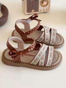 一双夏季凉鞋，编织鞋面，交叉绑带设计，小花朵图案，脚踝处蝴蝶结点缀，棕色鞋底。风格甜美复古，属于夏季时尚款，适合儿童日常、度假等场景，适合3-12岁儿童