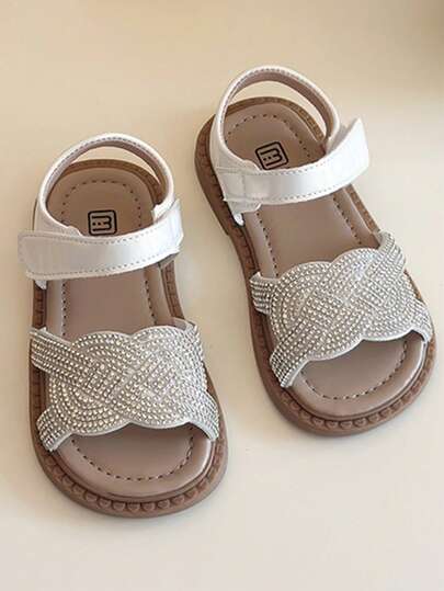 Un par de sandalias blancas para niños talla grande vendidas, con la Top blanca, un patrón trenzado de diamante de imitacións en la parte frontal, una correa blanca para el tobillo y una suela marrón. El estilo es elegante y brillante, pertenece al estilo de moda de verano, adecuado para el uso diario, vacaciones y otras escenas de los niños de 3 a 12 años