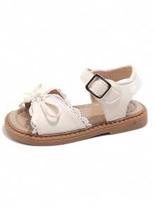 A Pair Of Popular White Children's Sandals With A White Strap And Metal Clasp On The Upper, A White Bow Trim And Lace Lace On The Front. The Style Is Sweet And Fresh, Belongs To The Summer Fashion Style, Suitable For Children's Daily, Holiday And Other Scenes, Suitable For 3-12 Years Old Children