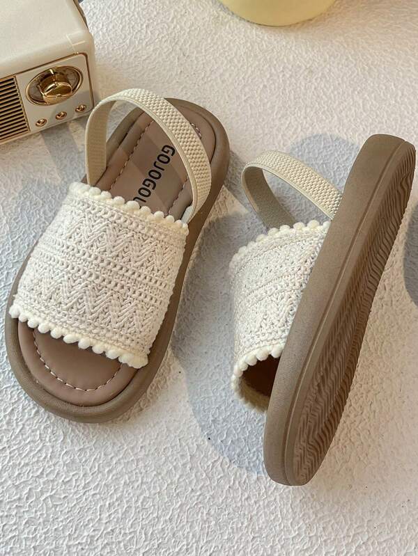 Un par de sandalias para niños. La parte superior está hecha de material de ganchillo de color crema y el borde está decorado con pompones. El diseño es exquisito y lindo, y se combina con un cinturón de gancho y bucle del mismo color. El estilo general es dulce y casual, adecuado para niñas de 3 a 12 años en el verano para viajes diarios, caminar y otras ocasiones para usar, puede mostrar la pura y encantadora elegancia.