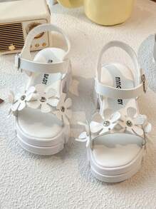 Un par de sandalias de plataforma blancas de moda de verano para niñas de 3 a 12 años, con elementos decorativos florales para un toque romántico. La parte superior es suave y cómoda, con diseño de gancho y lazo para un ajuste fácil, ya sea para juegos en interiores o paseos al aire libre, puede proporcionar un acompañamiento cómodo para los niños.