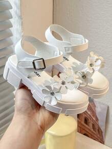 Un par de sandalias de plataforma blancas de moda de verano para niñas de 3 a 12 años, con elementos decorativos florales para un toque romántico. La parte superior es suave y cómoda, con diseño de gancho y lazo para un ajuste fácil, ya sea para juegos en interiores o paseos al aire libre, puede proporcionar un acompañamiento cómodo para los niños.