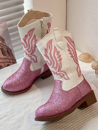 Un par de botas vaqueras de invierno para niñas. Los caños de las botas son blancos y están decorados con patrones bordados en rojo. La punta y las partes superiores están hechas de material rosa brillante, lo que le da un toque de lujo. El lateral de las botas está equipado con cremalleras para facilitar el calzado y el descalzado. El estilo general es de moda y llamativo, adecuado para niños de 3 a 12 años para combinar con faldas o pantalones.
