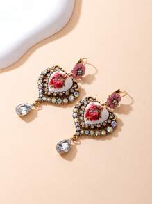 Il s'agit d'une paire de boucles d'oreilles bien conçues. Le style appartient à l'esthétique vintage et romantique, en mélangeant divers éléments : - Conception principale : Pièces en céramique en forme de cœur avec des motifs floraux rouges, ce qui donne une ambiance artistique et romantique. - Éléments décoratifs : les bords des formes de cœur sont garnis de nombreux strass scintillants, ajoutant une touche de luxe.