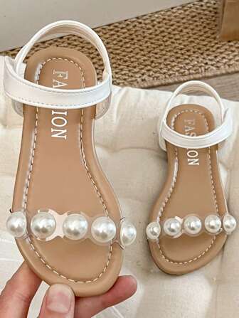 Un par de sandalias para niñas best-seller/2025. El Body principal del empeine es blanco, combinado con correas transparentes y decorado con perlas, presentando un estilo dulce y elegante. Este es un estilo de sandalia de perlas de moda para niñas, adecuado para que las niñas de 3 a 12 años usen en excursiones de verano diarias, asistir a fiestas y otras ocasiones, mostrando por completo el Charm de una princesa.