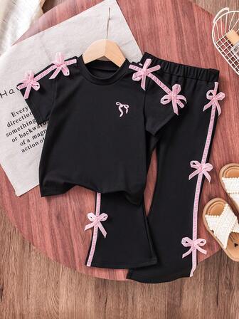 女童甜美酷炫芭蕾风黑色短袖T恤+喇叭裤套装。上衣肩部点缀俏皮粉色蝴蝶结，简约而不失活力。喇叭裤两侧饰有同色系蝴蝶结，时尚吸睛。适合休闲出游、朋友聚会，轻松打造甜美又不失性感的造型。