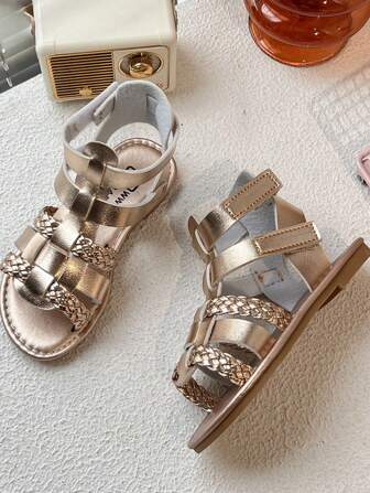 A Pair Of Best-Selling Children's /2025 New Girls' Sandals, With A Rose Gold Leather Upper, Features A Multi-Strap Cross Design, And Some Straps Are Woven, Presenting A Roman Style That Combines Fashion And Individuality. It Is Suitable For Girls Aged 3 To 12 To Wear In Their Daily Summer Outings, Plays And Other Occasions. It Belongs To The Fashionable Metallic Roman-Style Sandal Style For Girls.