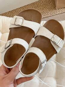 A Pair Of Children's /2025 New Girls' Sandals, With A Beige Matte Upper, Featuring A Double Strap And Metal Buckle Design, And A Wraparound Strap At The Ankle, Presenting A Simple And Fashionable Style.