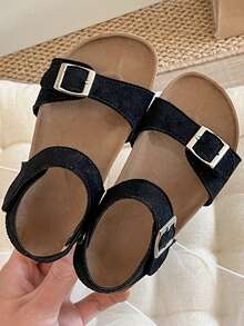 Ett par barnsandaler/flicksandaler från 2025 med svart matt ovandel, dubbel rem och metallspänne samt ett omlottband vid vristen, vilket ger en enkel och trendig stil. - Svart - Visa 7