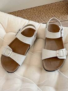 A Pair Of Children's /2025 New Girls' Sandals, With A Beige Matte Upper, Featuring A Double Strap And Metal Buckle Design, And A Wraparound Strap At The Ankle, Presenting A Simple And Fashionable Style.