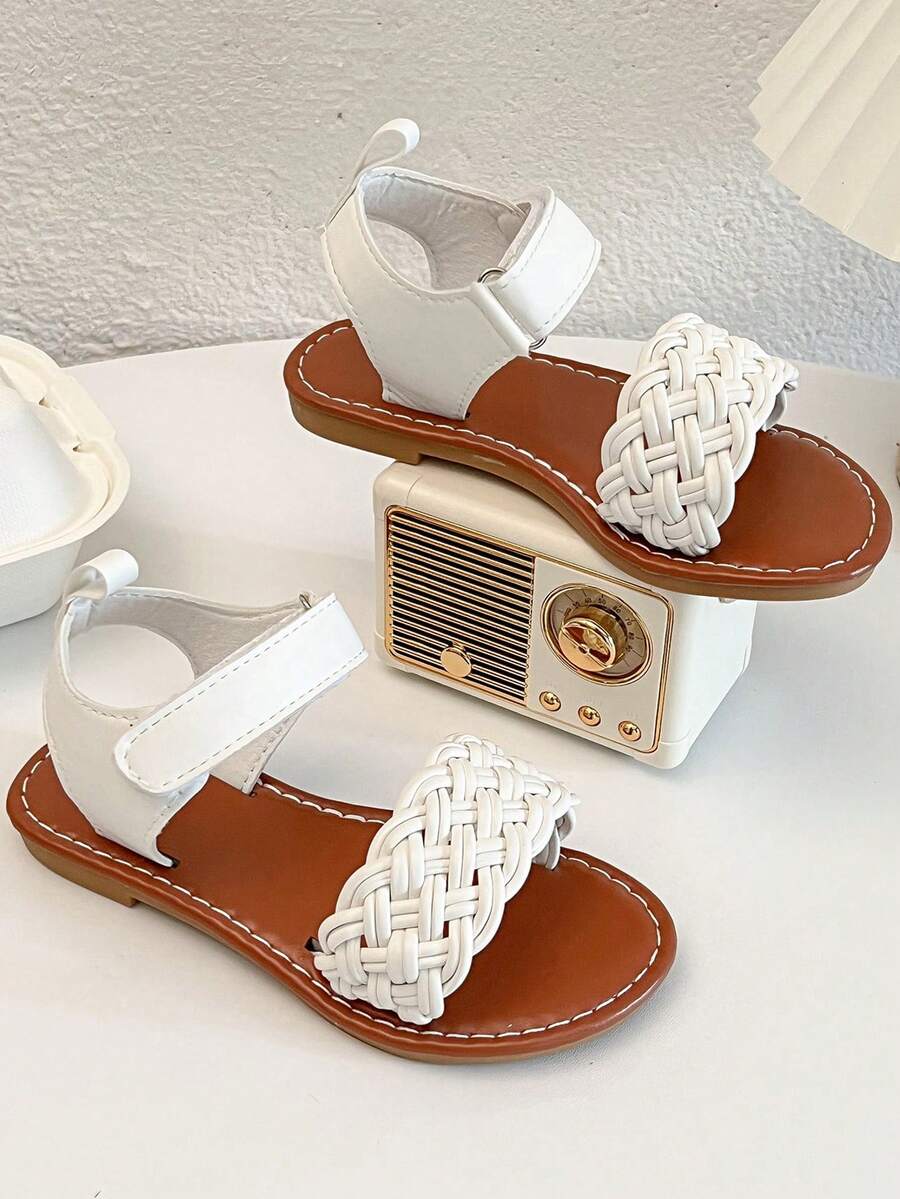 一双畅销儿童/女童凉鞋。鞋面采用白色皮革制成。前脚掌处有精致的编织图案，脚踝处有绑带。
