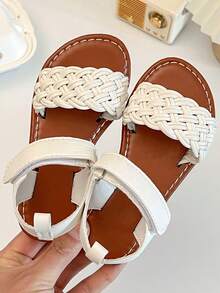 一双畅销儿童/女童凉鞋。鞋面采用白色皮革制成。前脚掌处有精致的编织图案，脚踝处有绑带。