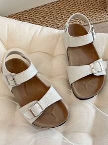 A Pair Of Children's /2025 New Girls' Sandals, With A Beige Matte Upper, Featuring A Double Strap And Metal Buckle Design, And A Wraparound Strap At The Ankle, Presenting A Simple And Fashionable Style.