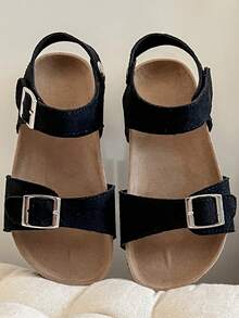 Ett par barnsandaler/flicksandaler från 2025 med svart matt ovandel, dubbel rem och metallspänne samt ett omlottband vid vristen, vilket ger en enkel och trendig stil. - Svart - Visa 4