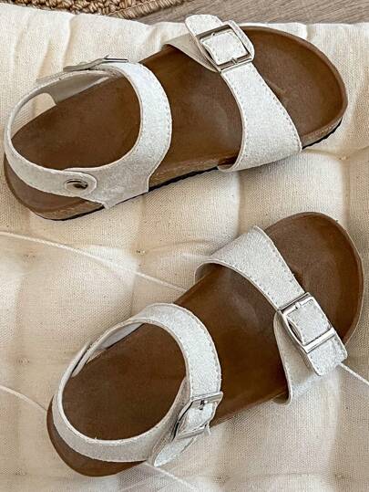 A Pair Of Children's /2025 New Girls' Sandals, With A Beige Matte Upper, Featuring A Double Strap And Metal Buckle Design, And A Wraparound Strap At The Ankle, Presenting A Simple And Fashionable Style.