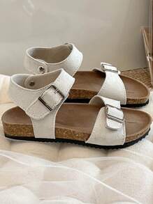 A Pair Of Children's /2025 New Girls' Sandals, With A Beige Matte Upper, Featuring A Double Strap And Metal Buckle Design, And A Wraparound Strap At The Ankle, Presenting A Simple And Fashionable Style.