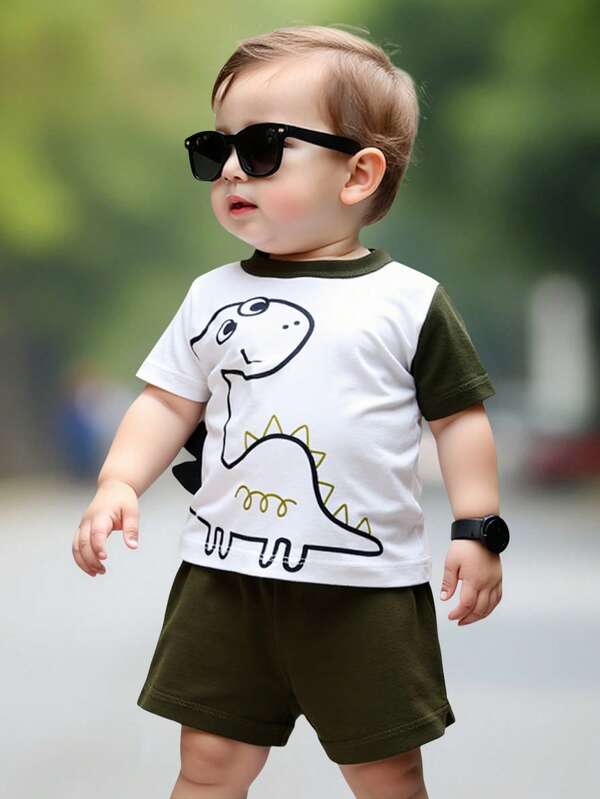 Set de dos piezas niños playera manga corta y short camiseta de manga corta blanca con mangas y cuello en color verde oscuro. En la parte frontal tiene un dibujo de un dinosaurio sonriente, con detalles en negro y amarillo, y unas pequeñas placas o picos en 3D sobresaliendo del costado, simulando las espinas dorsales del dinosaurio. Shorts verdes oscuros, de tela ligera con cintura elástica, diseñados para brindar comodidad al bebé o niño pequeño.
