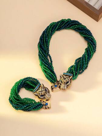 女士项链和手链套装，包含一条项链和一条手链，饰有渐变绿蓝珠子，并以镶嵌蓝色宝石和钻石的精致虎头扣点缀。独特的设计融合了粗犷与迷人的元素，适合搭配极简主义或前卫风格的服装，是派对造型的完美配饰，也是整体造型的焦点。