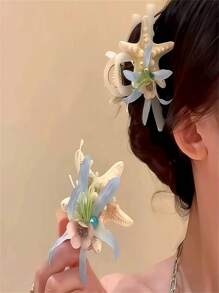 Um novo tipo de presilha de cabelo com flor de concha marinha, adequado para penteados durante férias na praia. Possui um formato de coque que fica na parte de trás da cabeça e vem com uma presilha de cabelo. O adereço de cabeça apresenta um design em forma de tubarão com um lado rosa e um lado azul. É um presente para as senhoras e adequado tanto para uso diário quanto para styling de moda.