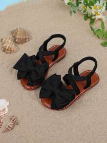 1 par de sandalias planas de unicolor para niñas, con diseño de tiras cruzadas con decoración de moño, y suela suave y cómoda, adecuada para salidas de verano, viajes a la playa y vacaciones de las niñas