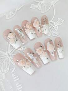 Un ensemble de 10 manucures en forme de cercueil longues et délicatement conçues, avec des pointes françaises blanches peintes à la main style Y2K, des feuilles d'argent et d'or brillantes, ainsi qu'un design 3D haut de gamme avec fleurs de camélia, strass et chaîne de perles de fantaisie.