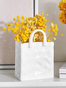 1件独特的白色和金色手提包造型树脂花瓶，这款时尚花瓶配有金属把手，非常适合在咖啡桌、梳妆台上或卧室装饰中展示鲜花，为您的家增添迷人的现代气息。