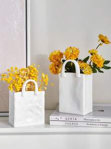 1件独特的白色和金色手提包造型树脂花瓶，这款时尚花瓶配有金属把手，非常适合在咖啡桌、梳妆台上或卧室装饰中展示鲜花，为您的家增添迷人的现代气息。