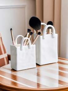 1件独特的白色和金色手提包造型树脂花瓶，这款时尚花瓶配有金属把手，非常适合在咖啡桌、梳妆台上或卧室装饰中展示鲜花，为您的家增添迷人的现代气息。