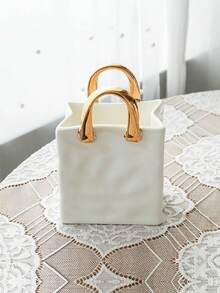 1件独特的白色和金色手提包造型树脂花瓶，这款时尚花瓶配有金属把手，非常适合在咖啡桌、梳妆台上或卧室装饰中展示鲜花，为您的家增添迷人的现代气息。