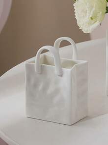 1件独特的白色和金色手提包造型树脂花瓶，这款时尚花瓶配有金属把手，非常适合在咖啡桌、梳妆台上或卧室装饰中展示鲜花，为您的家增添迷人的现代气息。