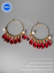 Un par de pendientes originales de perla. Estos pendientes exquisitamente diseñados presentan un aro dorado como Body principal. Enhebradas meticulosamente a lo largo del aro hay siete cuentas de cristal rojo natural con forma de gota. Acentuando estos, hay dos perlas barrocas, lo que crea un impresionante contraste con el ardiente atractivo de los cristales rojos.