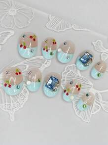 Coffret nail art comprend 10 ongles courts en amande faits main, avec un style French manucure bleu, des cerises peintes à la main et des strass carrés bleus, le tout pour un éclat brillant. Fabriqués selon le nouveau style Ballet Nail.