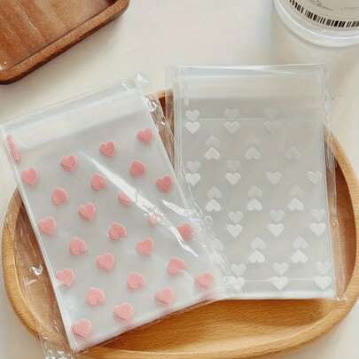 100个透明心形自粘包装袋，适用于饼干、糖果和甜点，也适合礼品和纪念品包装，是情人节、婚礼和其他庆祝活动的理想之选。