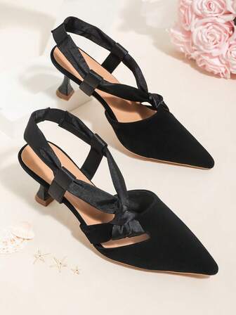 Eleganta svarta slip-on-pumps med spetsig tå och satinrosettdekoration, asymmetriska klackar, lämpliga för pendling eller lättare sociala tillfällen.