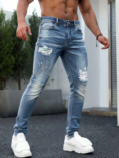 Jeans skinny para hombre en denim azul claro, con detalles de roturas y salpicaduras, estilo urbano y creativo