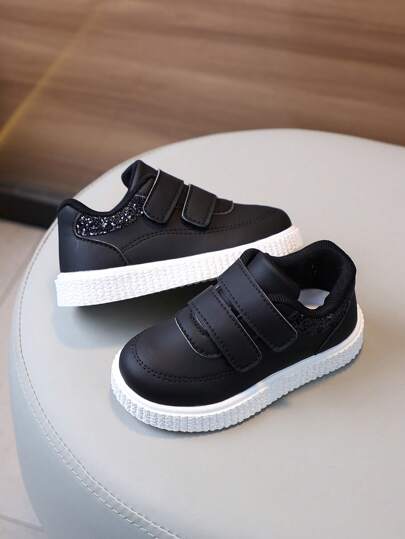 一双纯色PU时尚儿童运动鞋，轻盈柔软的白色运动鞋。采用便捷的双钩环扣设计，并饰有闪亮亮片。这款一脚蹬鞋适合男孩和女孩全年穿着。