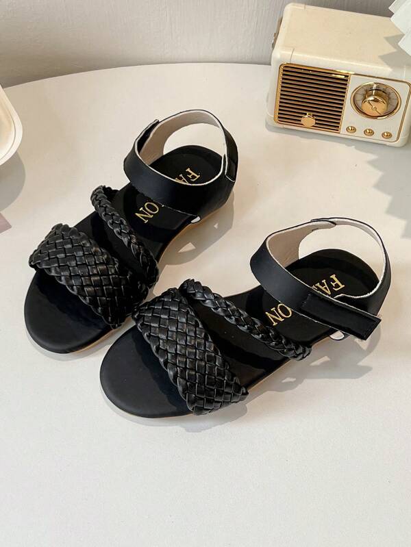 Un par de sandalias planas para niñas con correas tejidas, en un estilo sencillo y casual, adecuadas para salidas diarias