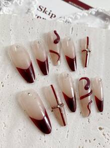 Neujahrsnägel. Mit einem süßen, kühlen, prächtigen und eleganten Stil sind dies handgefertigte 10 Stücke lange mandelförmige gepresste Fake-Nägel. Die Grundfarbe ist ein sanftes Nude-Rosa, mit handbemaltem weinrotem Französisch-Stil, roten Kreuzlinien, leicht luxuriösen Stahlperlen und Diamantdekorationen.