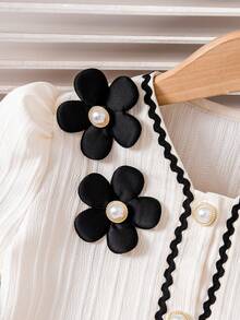 Young Girls Elegant Outfit - Short Puff Sleeve Top Paired With High-Waisted Skirt. The Puff Sleeve Design On The Top Is Playful And Cute, Flattering The Arm Line. The Multi-Layer Skirt Sways Gracefully When Moving. The White Main Color Is Fresh And Refined, With Delicate Black Lace And Floral Accents, And Faux Pearl Elements Adding An Elegant And Sophisticated Touch.