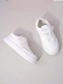 زوج من أحذية رياضية بيضاء بسيطة ذات لون أحادي من مواد ناعمة وقابلة للتنفس بأصابع مستديرة وكعب منخفض للاستخدام اليومي والمدرسة