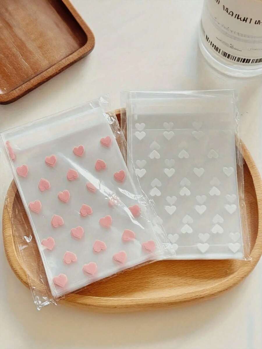 100个透明自粘心形包装袋，适用于饼干、糖果和甜点，适合礼品包装，是情人节、婚礼和其他新年节日送礼的理想选择。