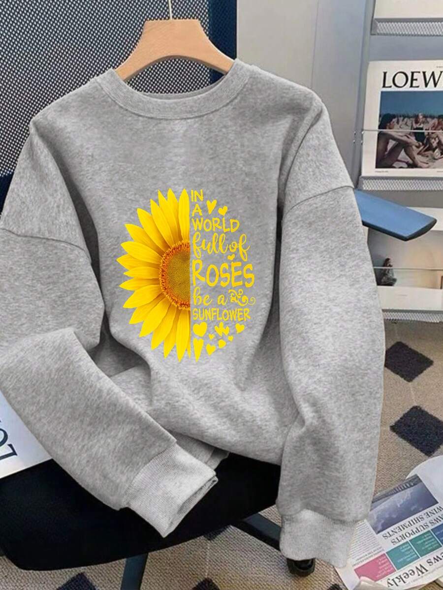 Um mundo cheio de rosas Seja um girassol O moletom apresenta um design de girassol amarelo brilhante com pétalas irradiando para fora O texto é organizado em um padrão circular ao redor do girassol em fonte preta contra o fundo bege do moletom O estilo geral é casual e confortável Perfeito para uso diário A impressão transmite uma pose
