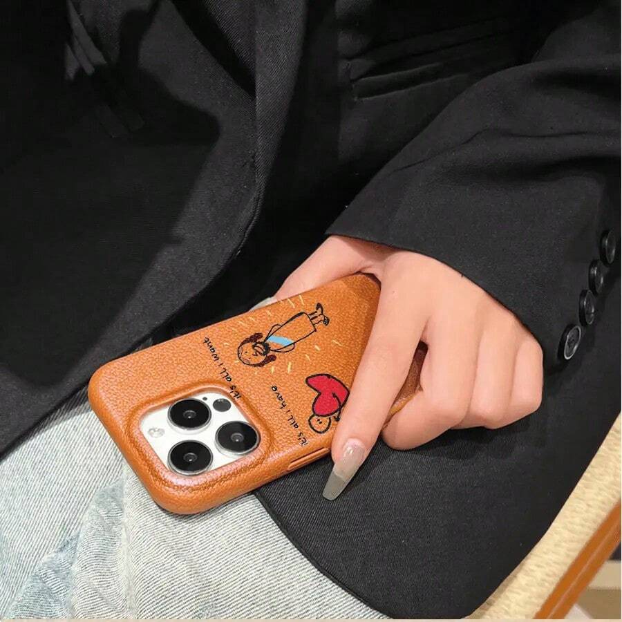 Teléfono con textura de lichi y estampado de una personita con un corazón lleno de amor. Compatible con phone 16 Pro Max, 16, 15 Pro, 14, 14 Plus, 13, 13 Pro, 12 Pro y 12 Pro Series. Resistente al desgaste y a las huellas dactilares. - Marrón - Ver 1