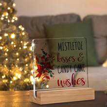 Articole decorative de Crăciun, inclusiv ornamente din acadele pentru casă, sărutări și urări cu tematică de vâsc, afișate pe semne și plăcuțe de birou din acril.