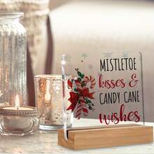 Articole decorative de Crăciun, inclusiv ornamente din acadele pentru casă, sărutări și urări cu tematică de vâsc, afișate pe semne și plăcuțe de birou din acril.