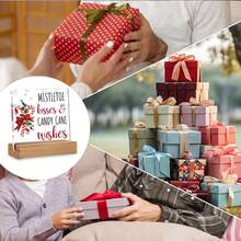 Articole decorative de Crăciun, inclusiv ornamente din acadele pentru casă, sărutări și urări cu tematică de vâsc, afișate pe semne și plăcuțe de birou din acril.