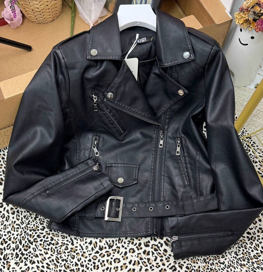 chaqueta estilo biker confeccionada en material de con textura firme, resistente y un ligero brillo. Presenta un clásico cuello amplio con detalles de tachuelas metálicas que aportan un aire rebelde; el cierre frontal asimétrico con cremallera y los múltiples bolsillos con cremalleras combinan practicidad con estilo. En la parte inferior incluye un cinturón ajustable con hebilla metálica que define la silueta y aporta un acabado más estructurado. Su diseño de inspiración rockera es versátil y moderno, ideal para looks de diario, salidas nocturnas, conciertos o festivales.