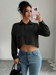 Blusa de manga larga es de color negro y tiene un estilo moderno y casual, Color: Negro, Estilo: Es una camisa de corte crop (corta), que deja al descubierto la parte superior del abdomen, Diseño: Tiene un cuello de camisa (o cuello clásico), Cierre: Cierre de botones en la parte delantera, Tejido: El material parece tener una textura sutil de líneas verticales (puede ser acanalado o con un tejido de rayas finas en la tela), Bolsillos: Presenta un bolsillo de parche sencillo en uno de los lados del pecho, Ajuste: Es de corte holgado o relajado en el cuerpo y las mangas, Manga: Manga larga con puños. - Negro - Ver 3
