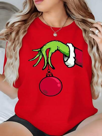 Mano verde sujetando esfera roja que simboliza travesura y espíritu de Navidad perfecta para fiestas camiseta de mujer 100% algodón