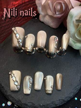 Set complet de unghii lucrat manual, cu 10 bucăți, cu unghii scurte în formă de sicriu, de culoarea șampaniei, tip ochi de pisică, cu vârfuri metalice franceze, strasuri 3D decorative pentru primăvară și vară, potrivit pentru fete, pentru a fi purtat zilnic și pentru a participa la întâlniri, petreceri tematice de Anul Nou și alte evenimente. Vine cu 1 pilă de unghii mică și 1 etichetă adezivă față-verso.